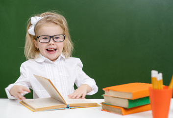 Girl at school in the classroom, sitting on the background of a green blackboard and reading a book
