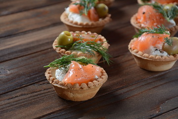 Tartalets with fresh salmon, philadelphia cream cheese, olives on wooden background