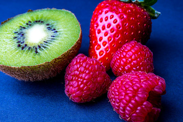 Kiwi, Erdbeere und zwei Himbeeren in einer Nahaufnahme vor grauen Hintergrund.