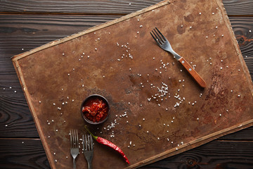 Top view of chili sauce with salt and forks on stone board on wooden surface