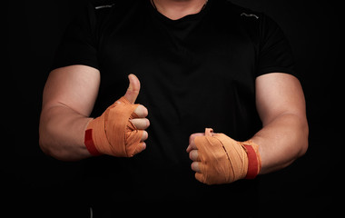 muscular athlete in black uniform shows a like, palms wrapped in orange textile sports bandage