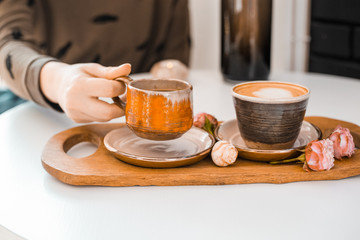 Girl's hand takes a cup of coffee from a wooden tray decorated with rosebuds located on a white table