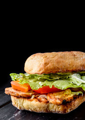 italian ciabatta panini sandwich with chicken, cheese and tomato on black wooden table