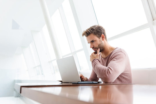 Image of young bearded man using laptop computer in cafe indoors