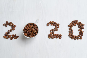Abstract figures 2020 from coffee beans and white cups on a wooden background.