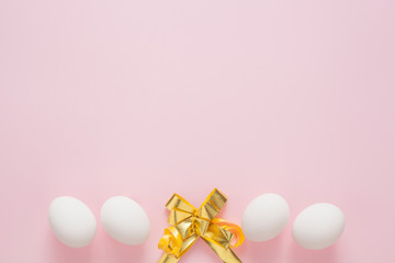 White eggs on a pink background, decorated with a gold bow, with copy space. Easter concept.