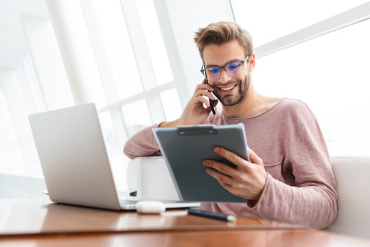 Image of man talking on cellphone and holding clipboard in cafe