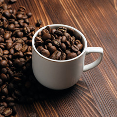 White cup with coffee beans against the background of a burnt wooden background. Square format.