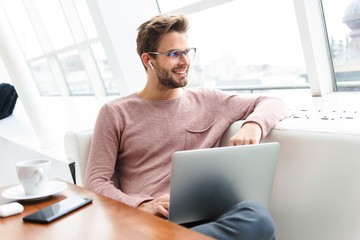 Image of man wearing earbuds working on laptop computer in cafe indoors