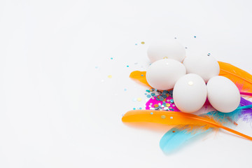 White eggs in colorful feathers and holiday sparkles, on a white background,  with copy space . Easter concept.