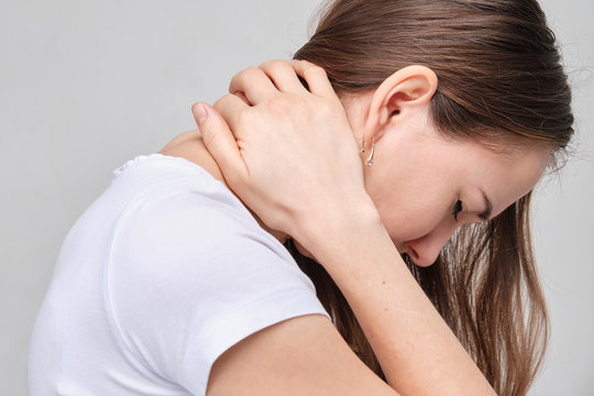 A girl in a white shirt massages her neck. Pain from osteochondrosis in the cervical spine.