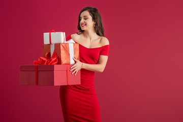 sexy, elegant girl holding gift boxes while smiling isolated on red