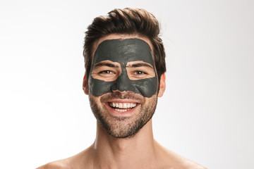 Photo of happy half-naked man with cosmetic mask on his face smiling
