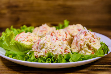 White plate with crab-cheese balls and lettuce leaves on wooden table