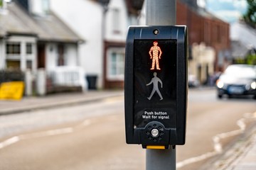 Pedestrian zebra crossing with an English text telling people to wait for appropriate signal and push the button. The blurred car in background is approaching © mino21