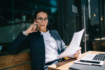 Female working with papers and talking on phone in cafe