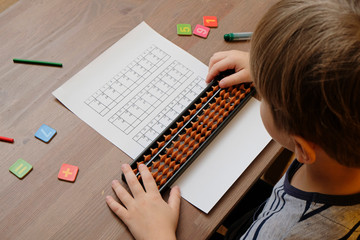 Little boy doing simple math exercises with abacus scores. Mental arithmeric. View from shoulder