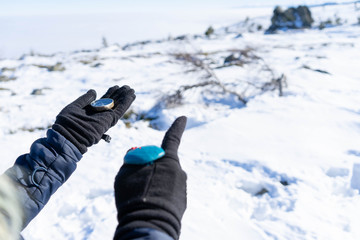 Mountaineer checking compass in a snow hill, lost on an exploration in the mountain. Hand pointing with finger direction, leading the way in the expedition. Finger show the direction to follow