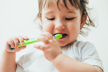 Little girl brushes her teeth with a toothbrush on a light background