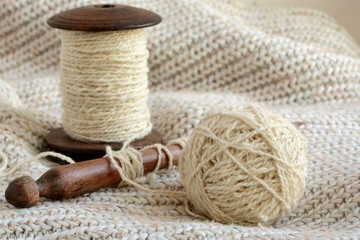 Ball of wool yarn, spool of thread and spindle on  background  of knitted sweater close-up.