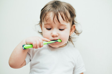 Little girl brushes her teeth with a toothbrush on a light background