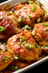 Roasted chicken thighs with mushrooms, garlic and herbs in a baking dish, close-up