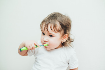 Little girl brushes her teeth with a toothbrush on a light background