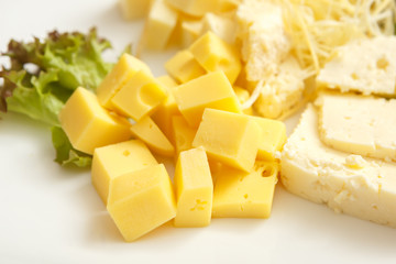 Cheese of different varieties cut into pieces and greens on a plate