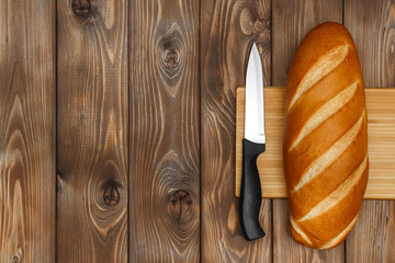 A loaf of bread on a cutting Board and a knife on a wooden background
