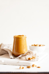 Obraz na płótnie Canvas Homemade natural paleo nut peanut cashew creamy butter in glass jar and spoon on white background. Copy space, vertical orientation