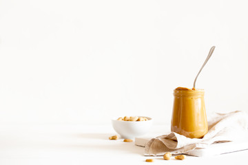 Homemade natural paleo nut peanut cashew creamy butter in glass jar and spoon on white background. Copy space, horizontal orientation