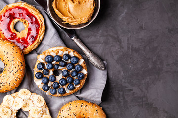 Variety of bagels with different toppings and natural paleo nut peanut cashew creamy butter on dark gray background. Healthy breakfast brunch concept. Top view,flat lay,copy space,horizontal orientati