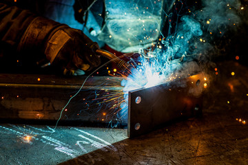 A welder in a metal factory welds metal parts, lights flash