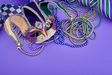 Colorful Mardi Gras mask on purple background with beads and ribbons. Top view. Copy space
