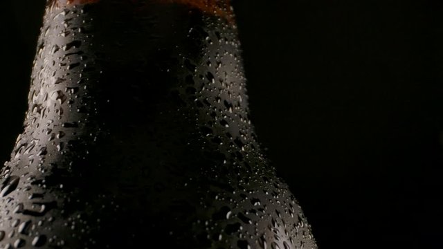 Pan right view of closeup wet bottleneck of glass bottle of fresh chilled beer in dark room.