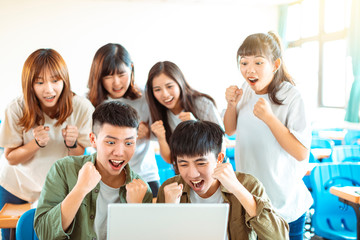 happy students looking at laptop  in classroom