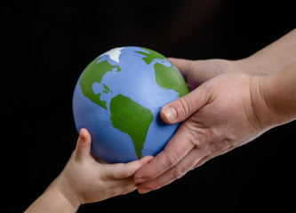 Close up hands of mother gives the planet into the hands of a child. Isolated on dark background