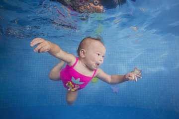 little girl in a pink swimsuit learns to dive underwater in the pool