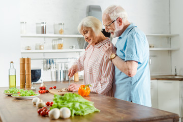 Side view of senior man embracing wife during cooking on kitchen table