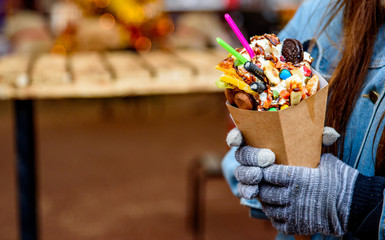 Young woman hands holding Hong Kong bubble waffle with ice cream, caramel syrup, fruits, chocolate