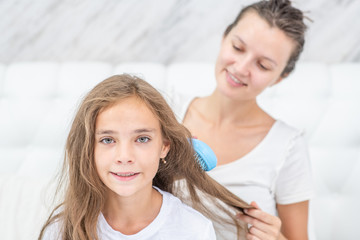 Smiling mom cares for her daughter's hair by combing it
