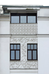 facade of a light-gray well-groomed plastered building with stucco in the form of grape leaves and circles, weaves, with ornament. Facade of a house with windows