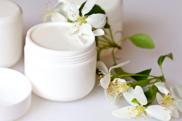 Fototapeta na wymiar Close up view on a white jar with cosmetic for face care and apple tree flowers on a white background. Spring still life, soft light, macro