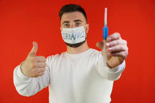 A Young Man In A Mask With The Inscription Coronavirus Holds A Vaccine In His Hand And Shows A Thumbs Up.
