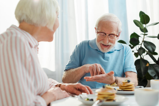 Selective focus of senior man talking to wife by coffee and pancakes on table - Powered by Adobe