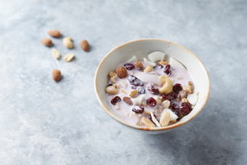 Bowl of granola with yogurt, nuts, cranberry and cocoanut on bright stone  background.