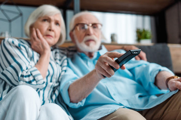 Selective focus of focused senior couple watching tv on couch in living room