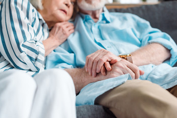 Obraz premium Selective focus of elderly couple holding hands while sitting on couch