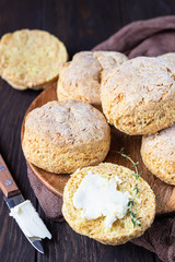 Wooden plate with English scones or buttermilk biscuits with cheese and thyme, dark brown wooden background.