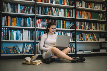 Smart woman smiling while working on laptop in library